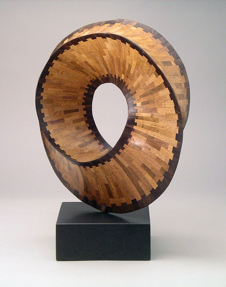 a segmented wood turning patterned wooden circle mounted on a black pedestal