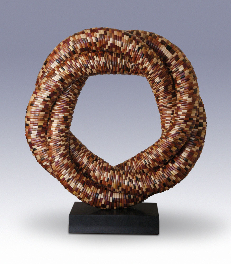 many segmented wood turning rings stacked together and braided into a standing ring