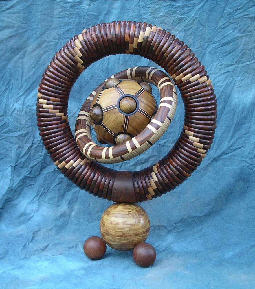 many dark segmented wood turning rings stacked in a larger ring orbiting a wooden sphere