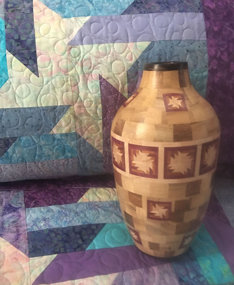 a patterned wooden vase on a patchwork quilt